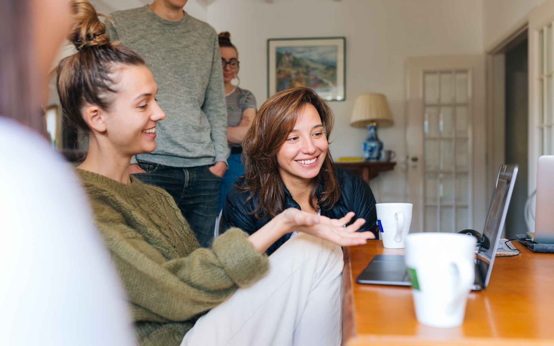 Group of young adults discussing home selling strategies around a table with laptops and coffee mugs, capturing a collaborative atmosphere.