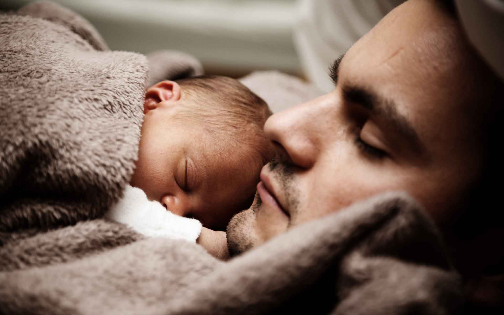 Father and newborn baby sleeping peacefully together, wrapped in soft blankets, symbolizing family comfort and togetherness.