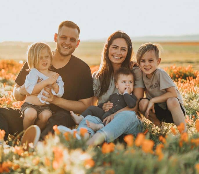 Family of five sitting together in a field of orange flowers, smiling and enjoying a sunny day.
