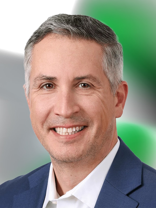Smiling professional man in a suit against a blurred green and gray background, representing expertise in mortgage lending and customer support.
